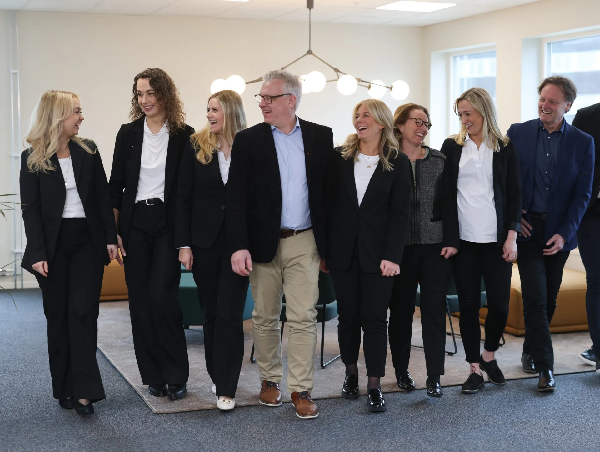 The Tacting team of nine colleagues walking together and smiling in a modern office.