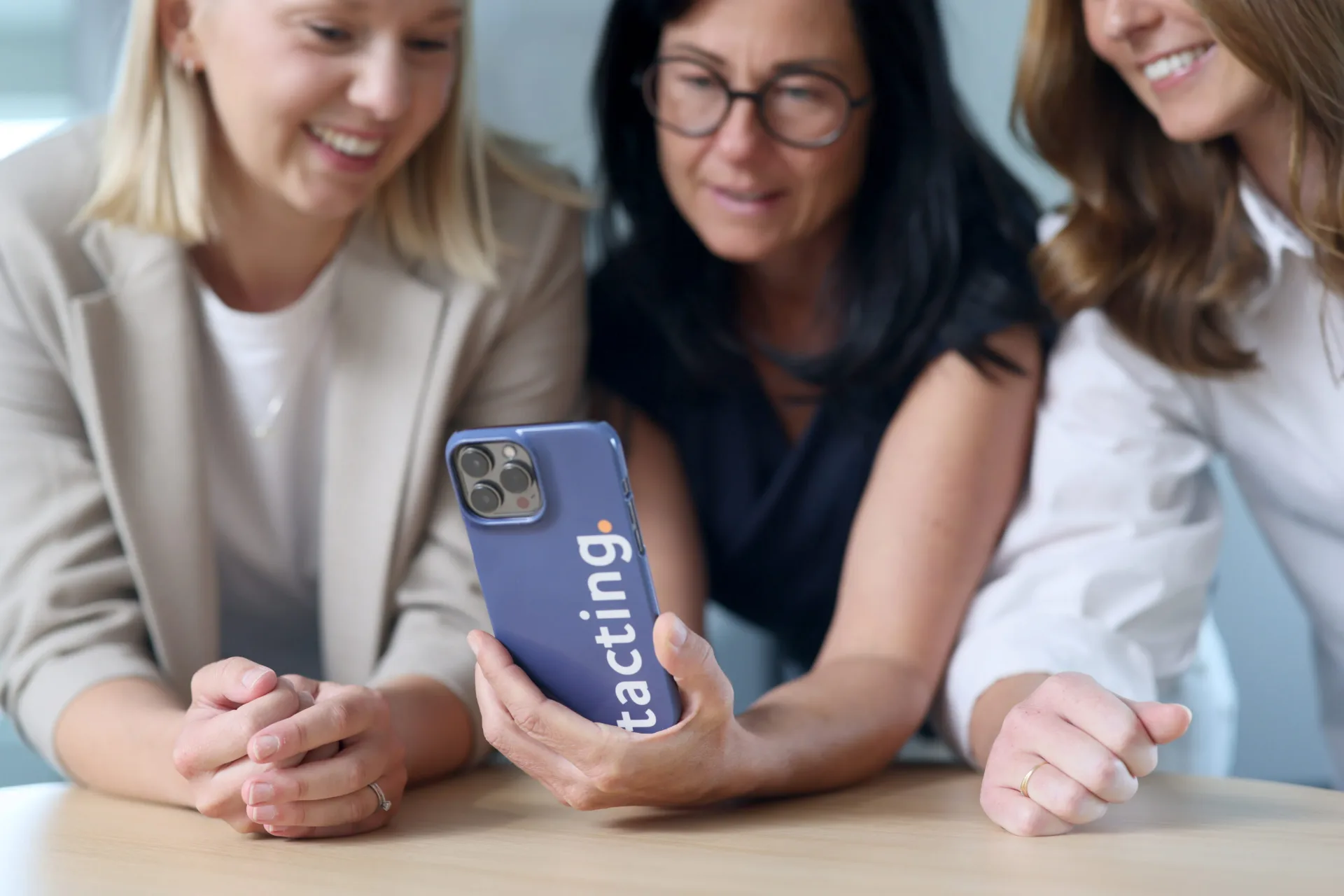 Three women looking at social media on a Tacting-branded smartphone.